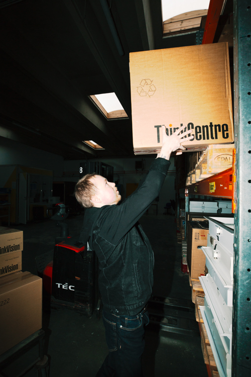 En lærling placerer en kasse på en hylde i lageret, lærling, lager, hylde, varerhåndtering, logistik, lagerarbejde