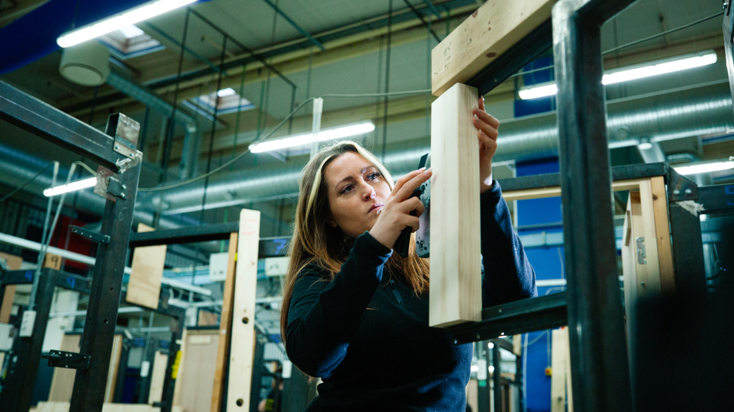 Kvinde arbejder med en træramme i et værksted under konstruktion, træramme, værksted, konstruktion, håndværk